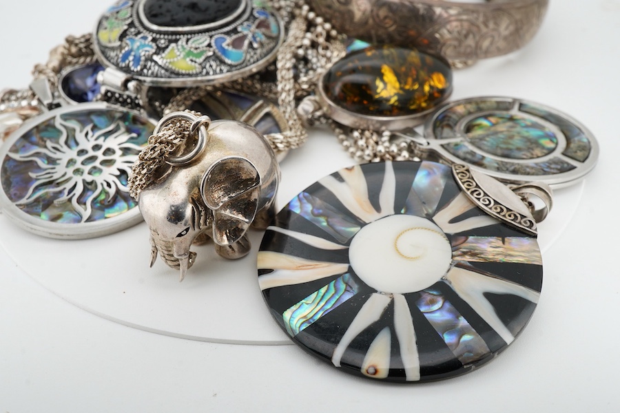 A collection of silver and costume jewellery, comprising: a pendant designed as an elephant; an enamel and porous black stone pendant; five shell medallion pendants; two paste pendants; and a treated amber pendant; all w